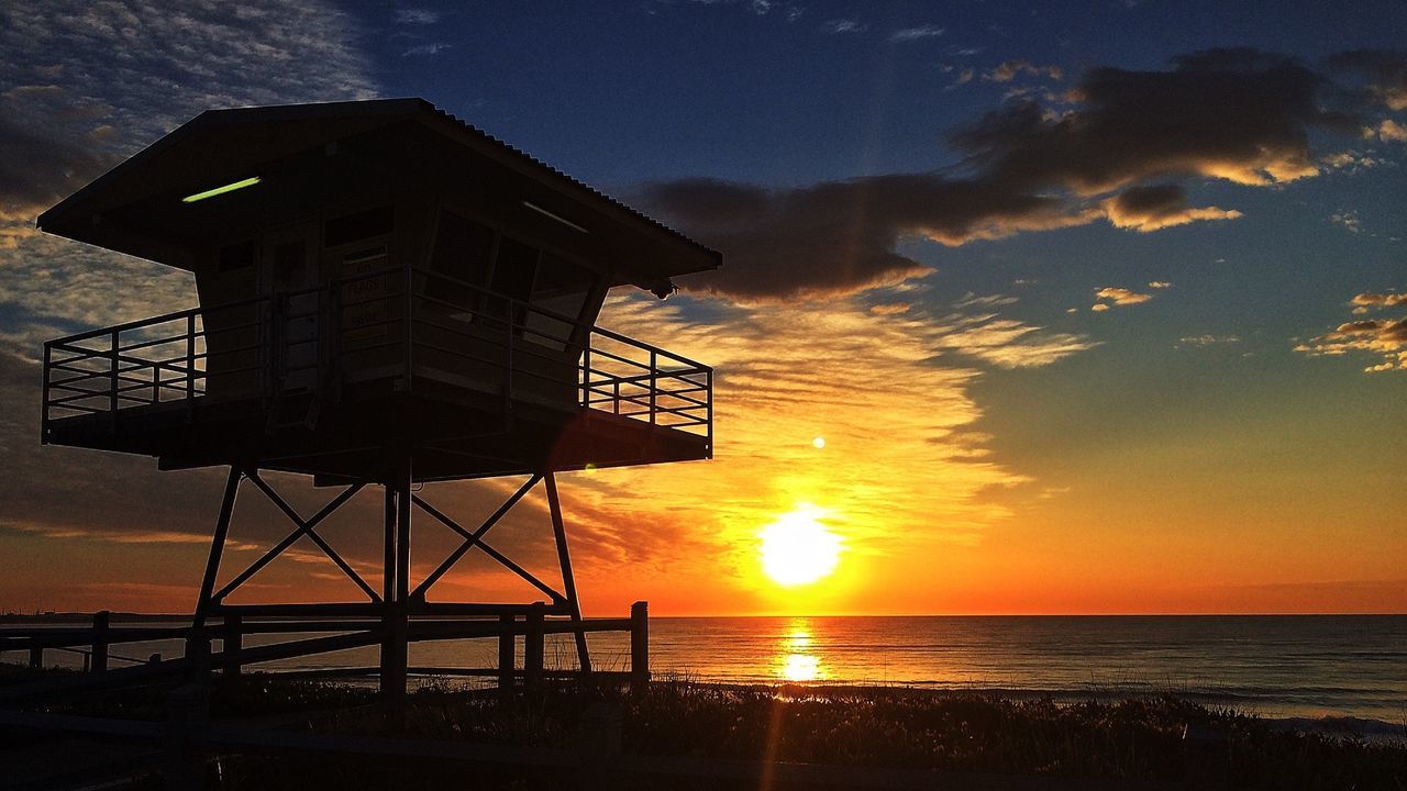Silhouette lifeguard tower at beach against sky during sunset