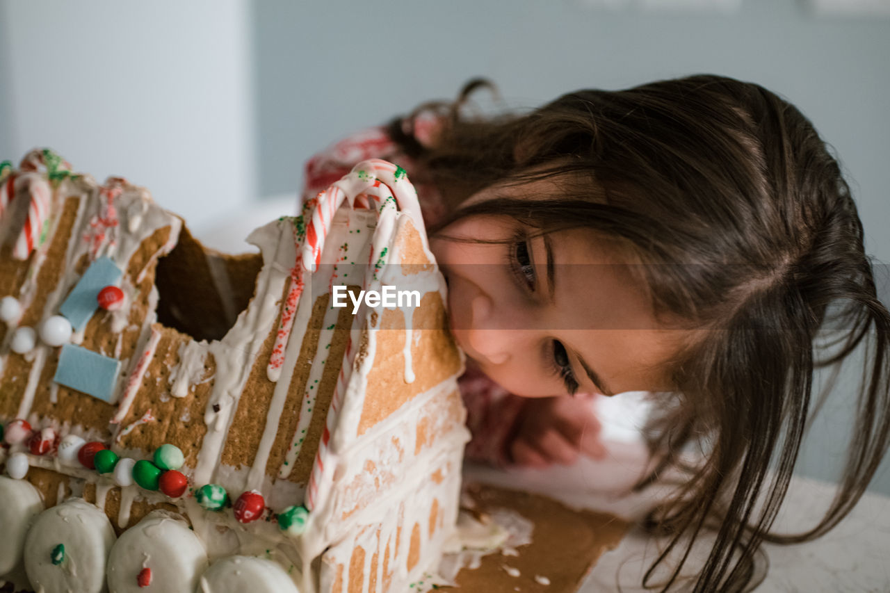 Young female child eating gingerbread house big bite