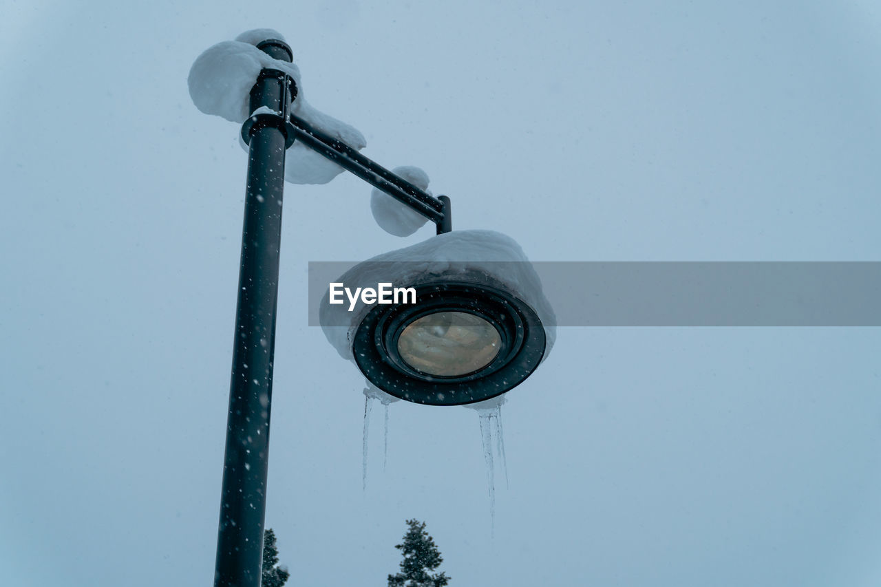 Low angle icicle-covered street lamp post in a snowy landscape against foggy sky in snow storm.