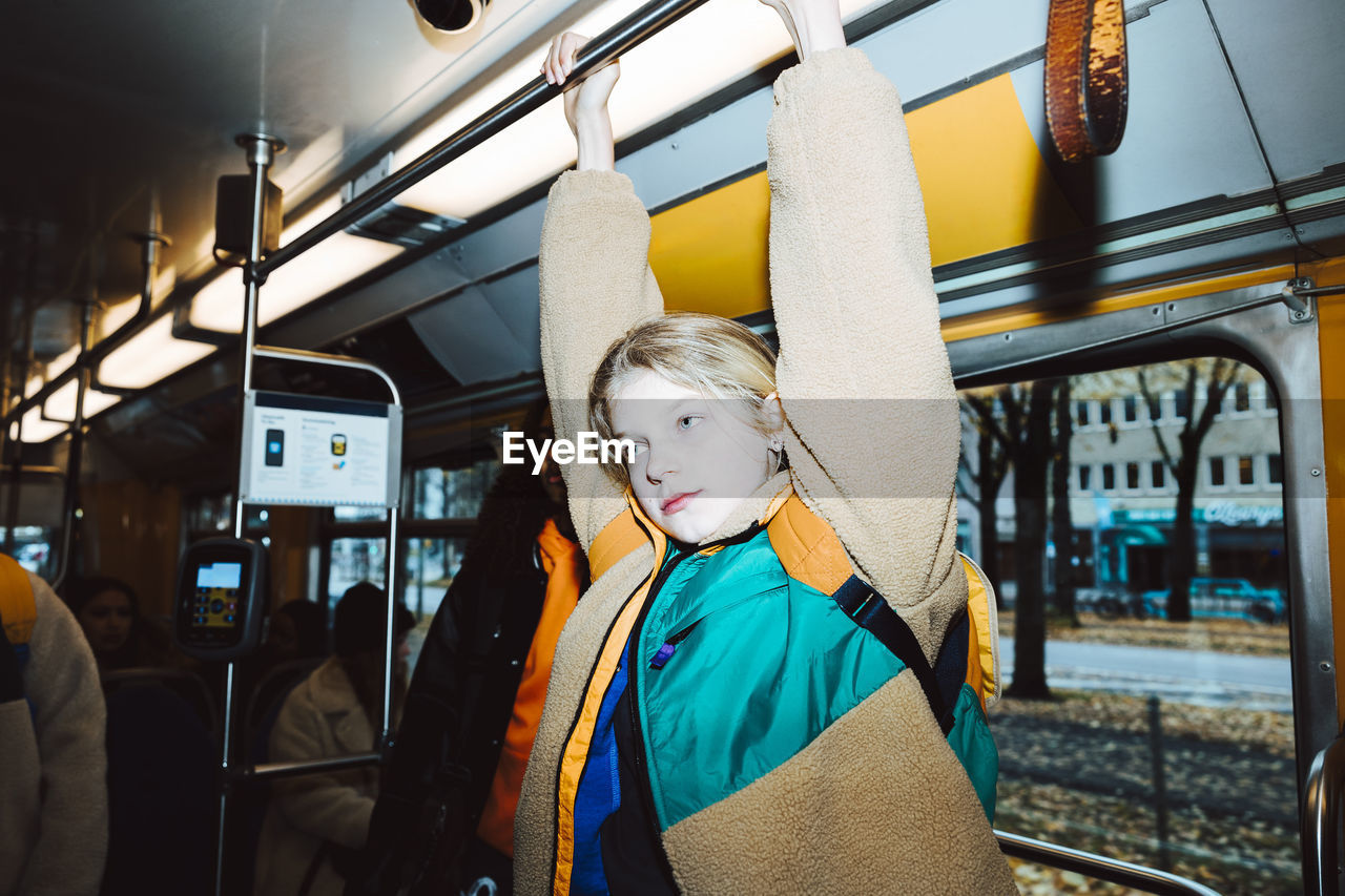 Girl holding handle while traveling in tram on weekend