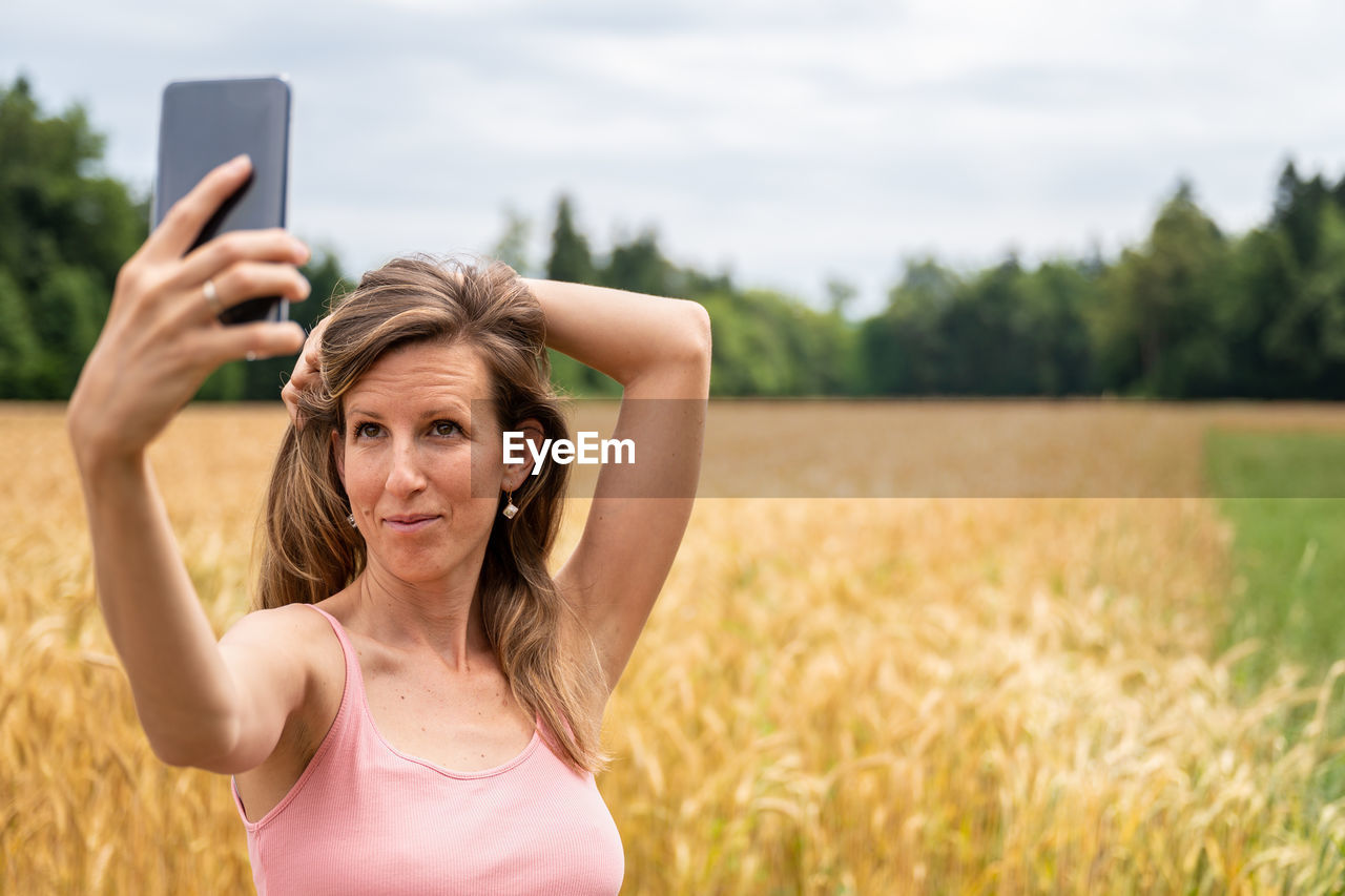 PORTRAIT OF SMILING WOMAN STANDING ON FIELD AT BEACH