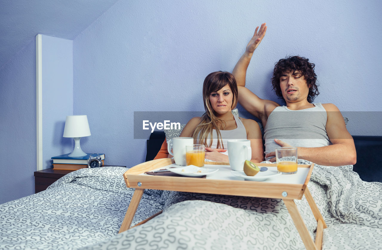 Young couple with food and drinks on bed at home