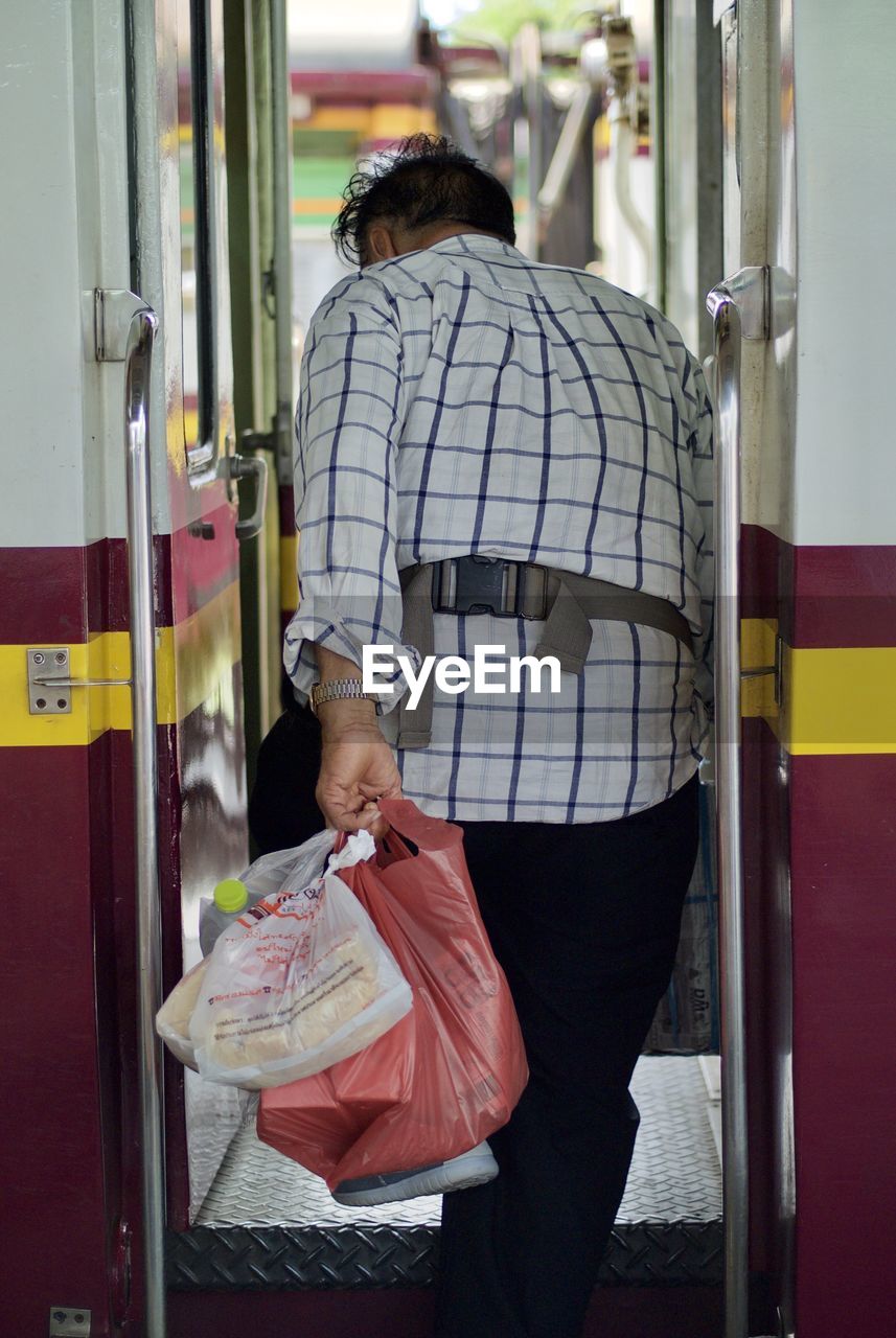 Rear view of man carrying plastic bags while entering train