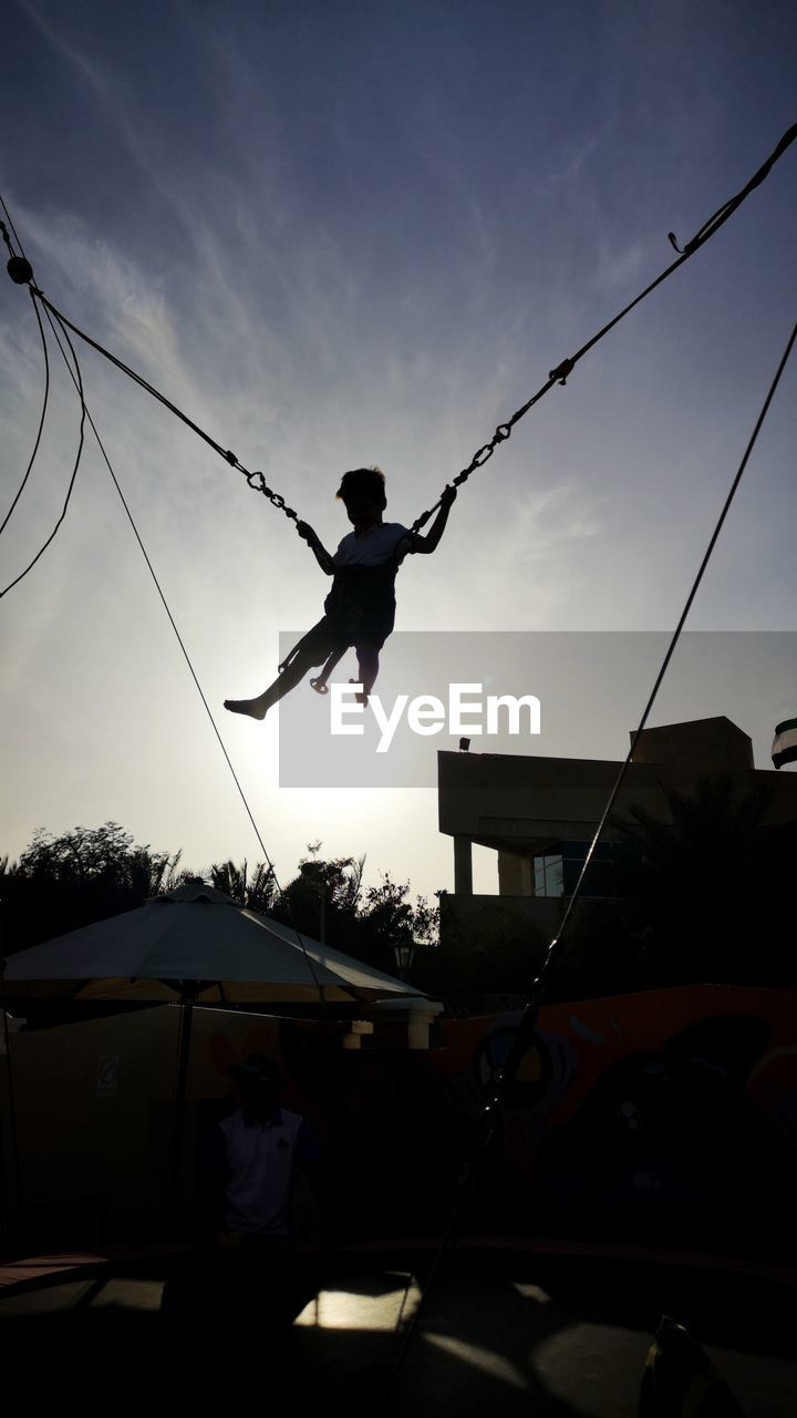 Silhouette boy on trampoline against sky during sunset