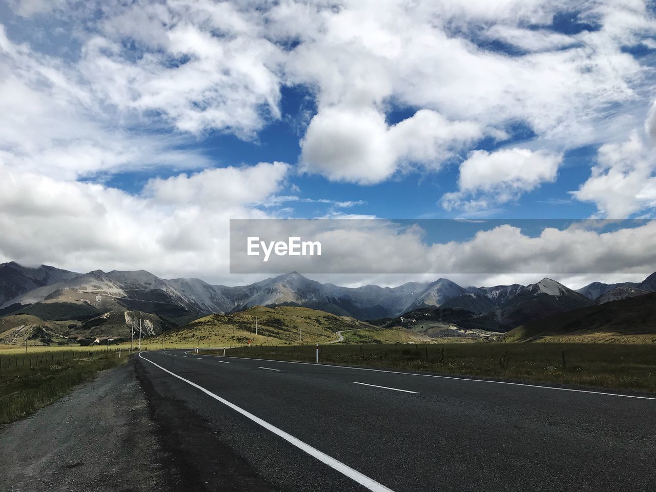 EMPTY ROAD BY MOUNTAINS AGAINST CLOUDY SKY