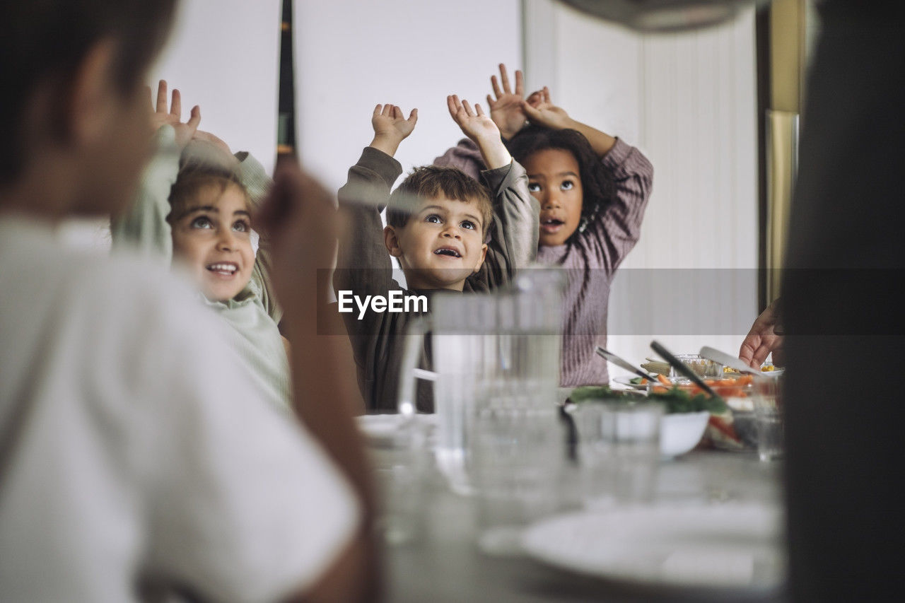 Happy children with arms raised during lunch time at kindergarten