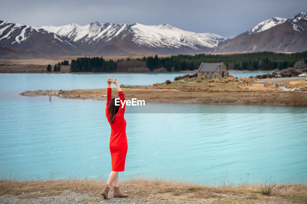 Asian female tourist pose at turquoise color lake tekapo with snowcapped mountain at the background