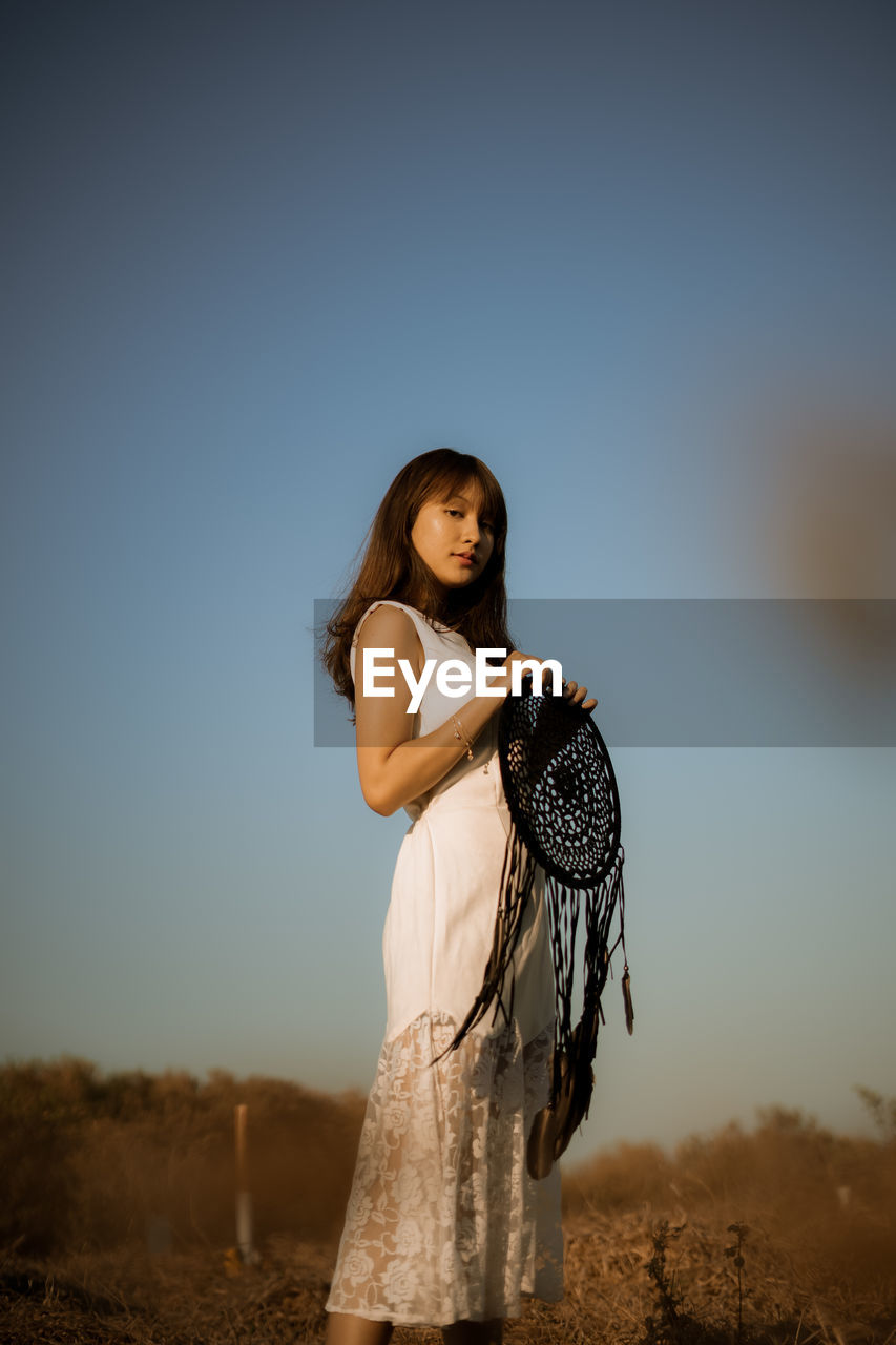 Side view portrait of woman with dreamcatcher standing against clear sky