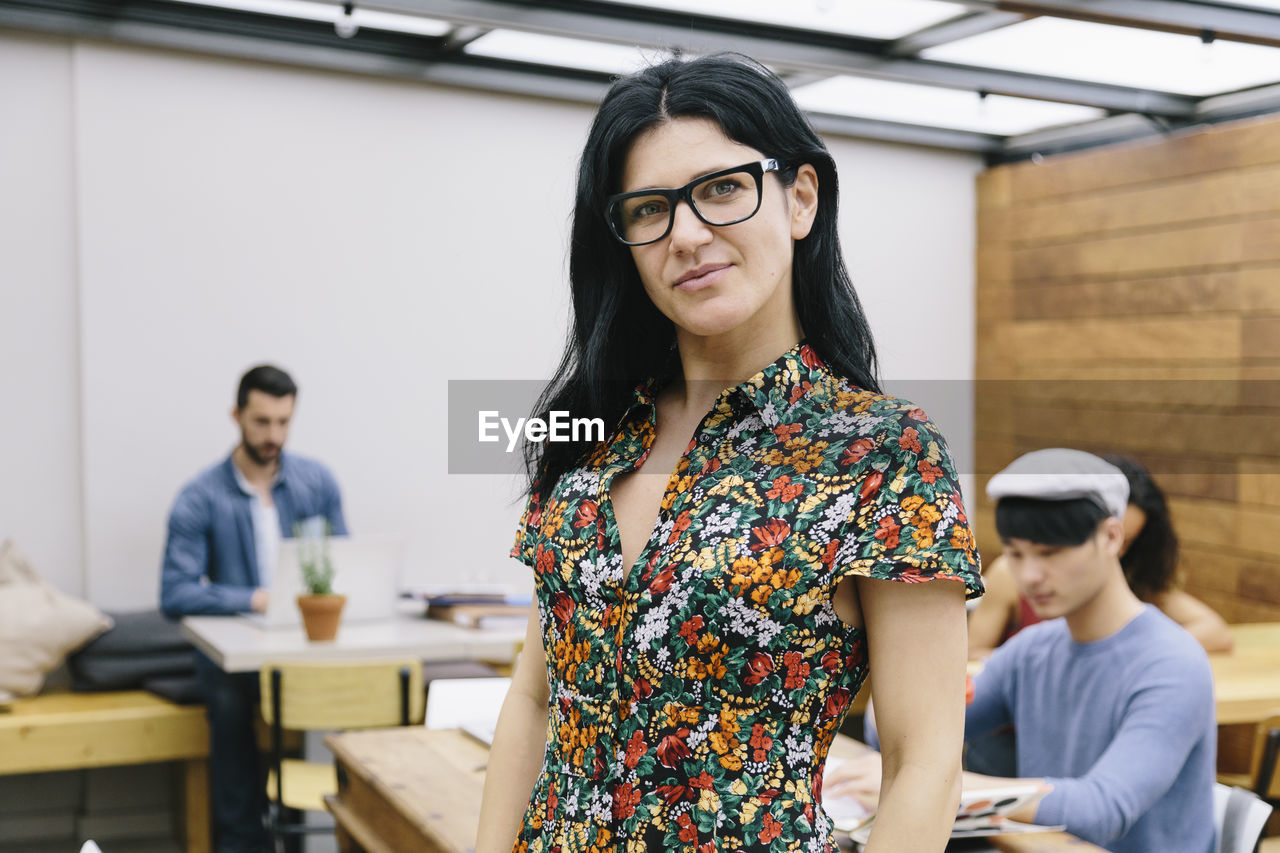 Young woman standing by table while colleagues working in background