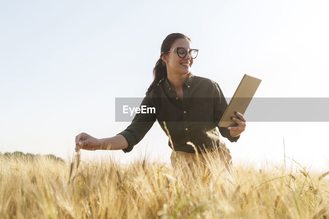 Happy businesswoman using tablet pc on barley field
