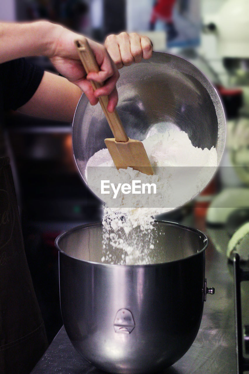 Cropped hands putting flour in container at kitchen