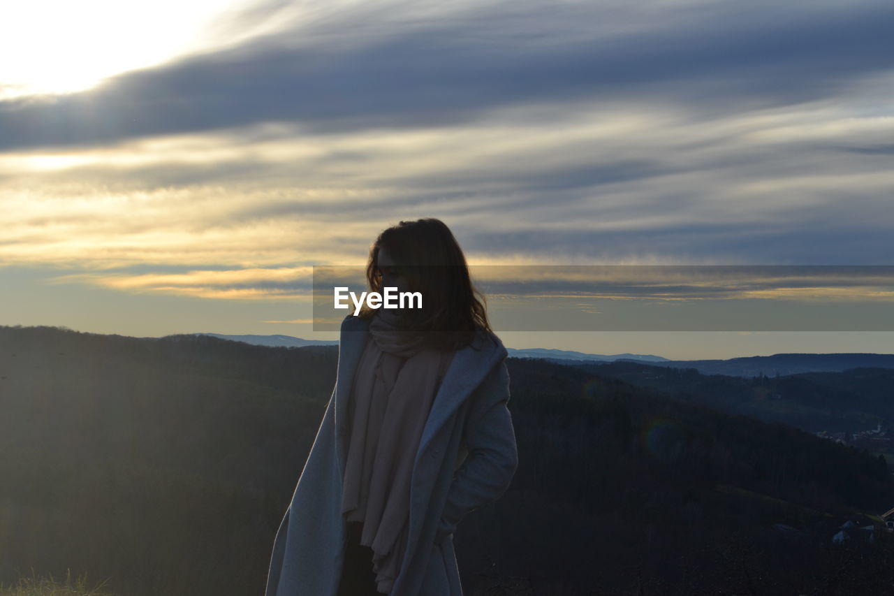 Young woman standing on mountain against sky during sunset