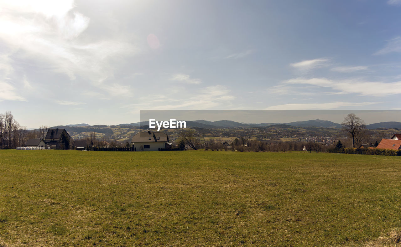 FIELD BY BUILDINGS AGAINST SKY