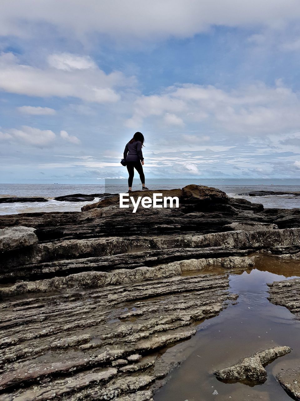 Rear view of woman standing on rock at beach against sky