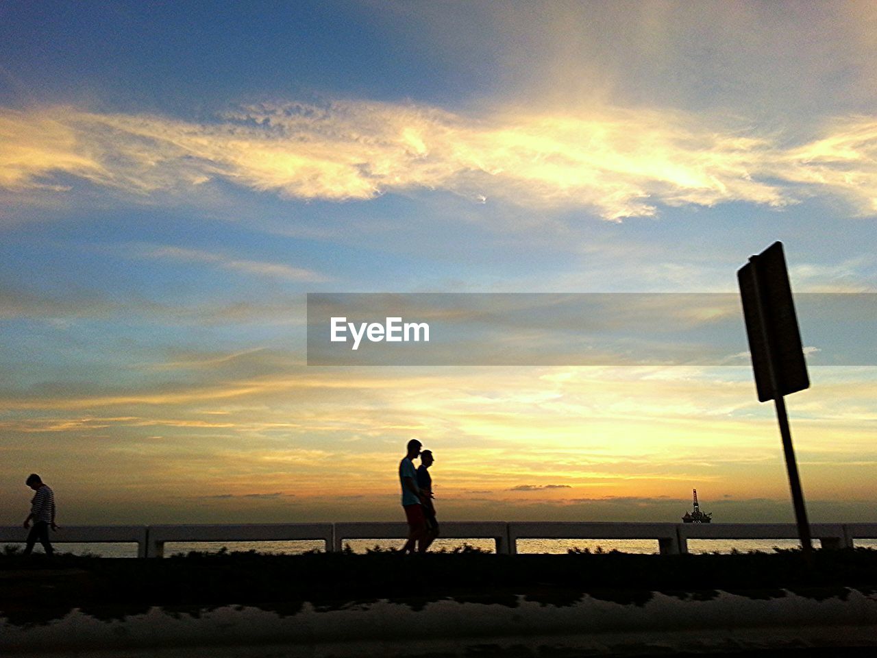 Side view of people walking against sea at sunset