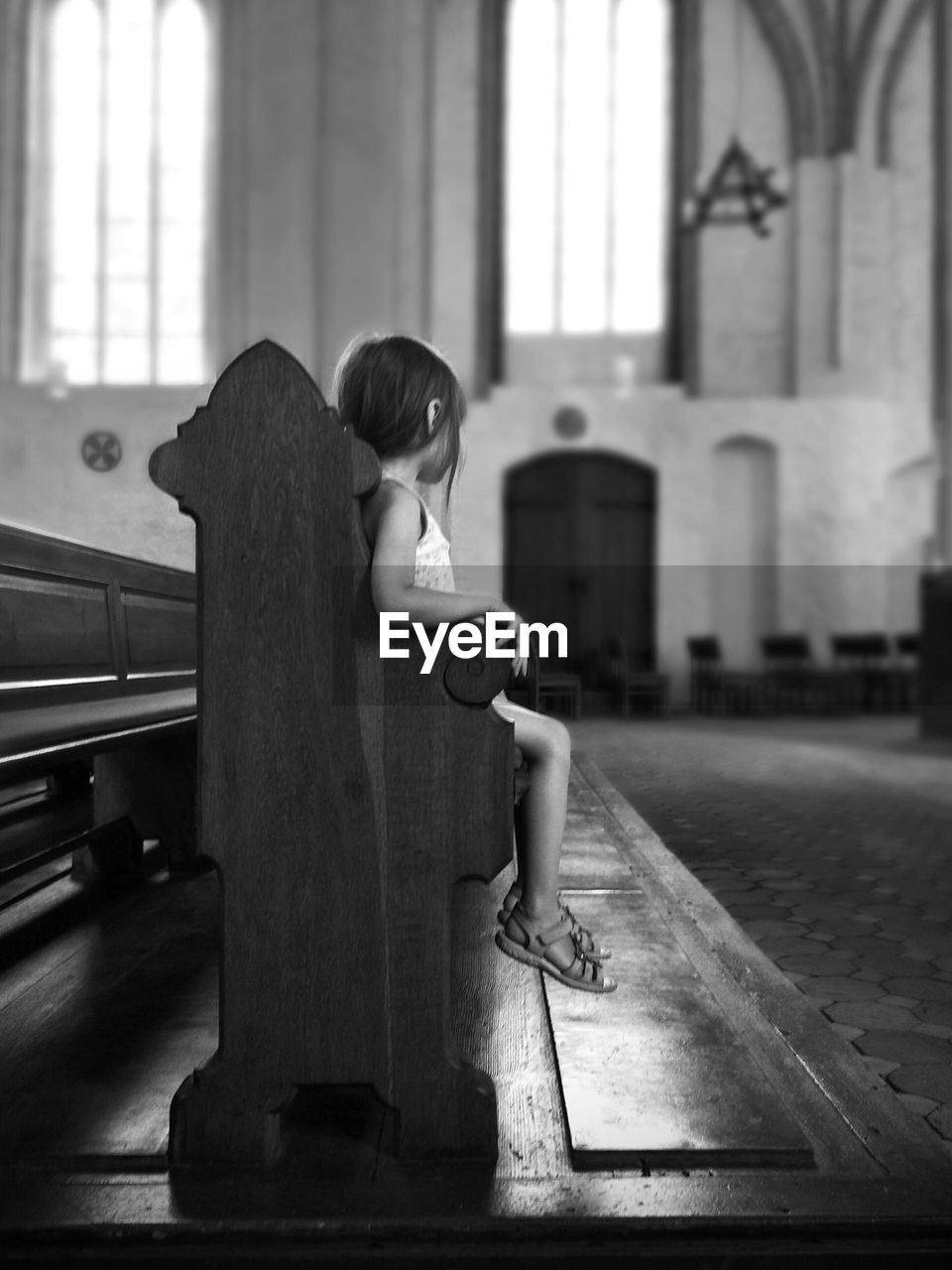 Side view of girl sitting on wooden bench in church