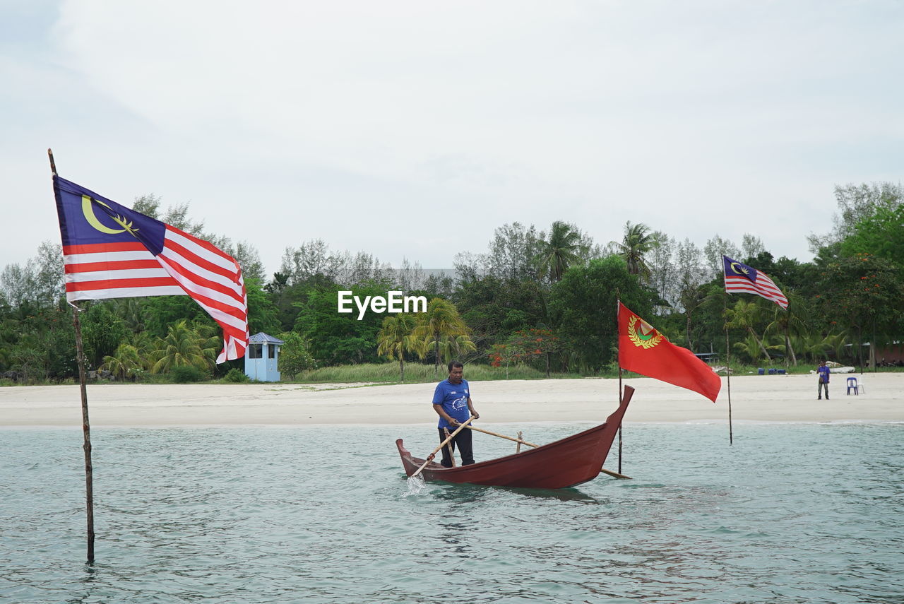 MEN ON BOAT IN SEA AGAINST SKY