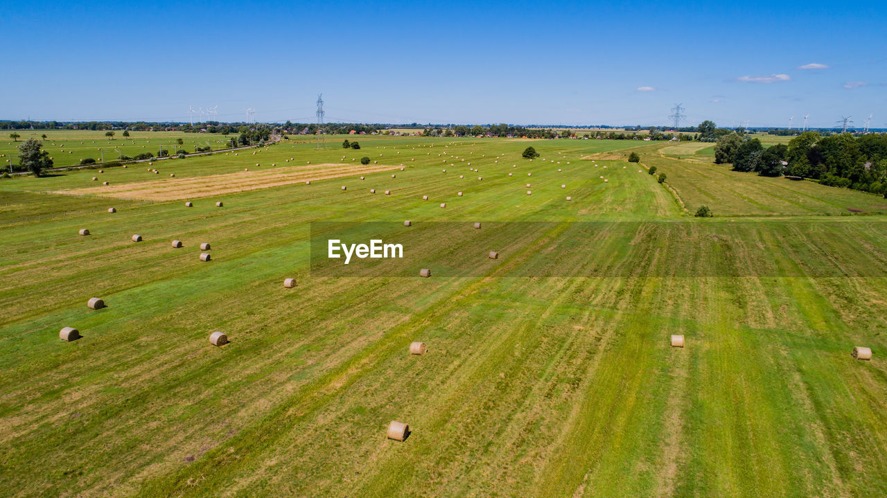 Hay bales on green landscape against blue sky