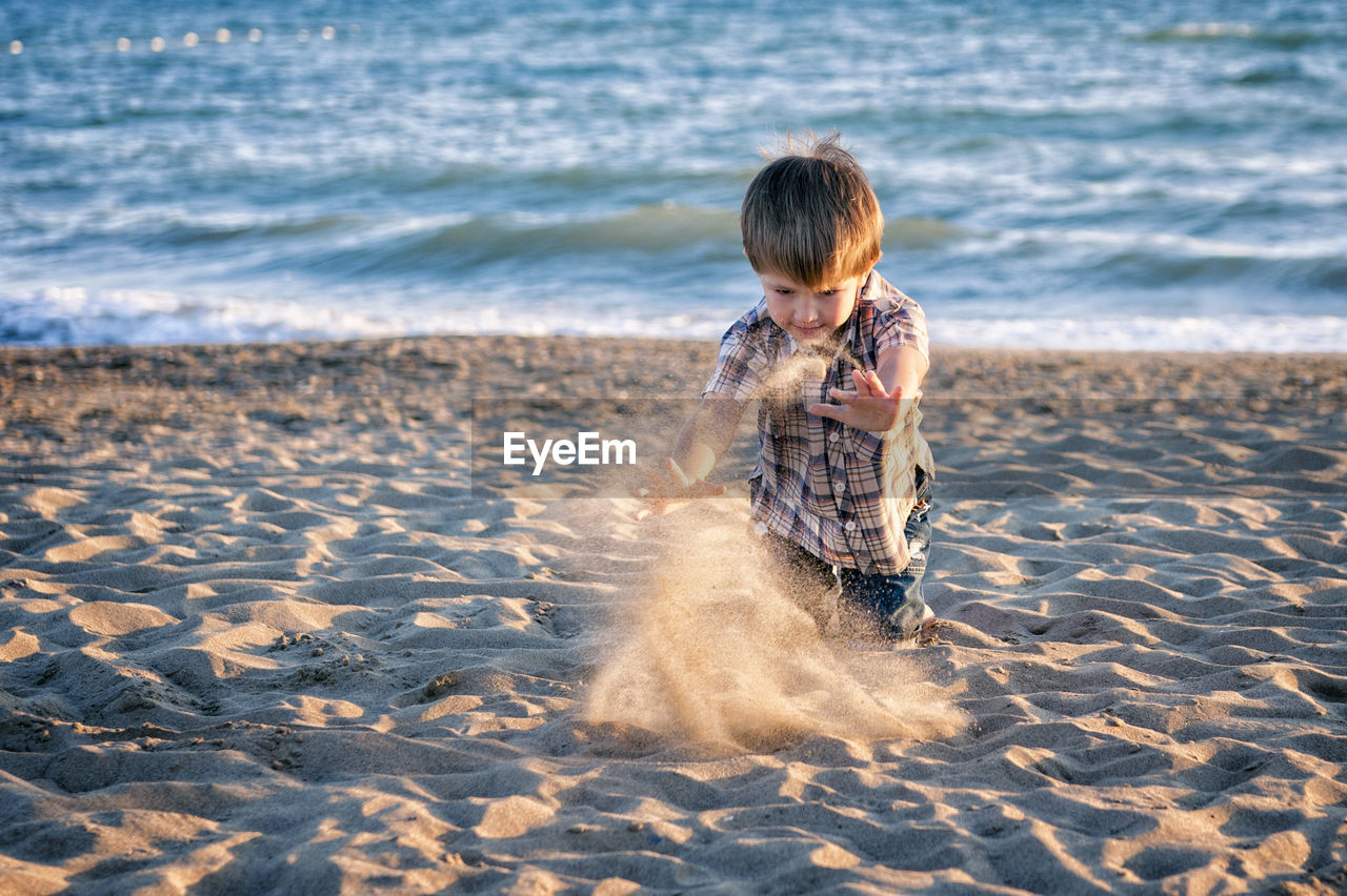 Boy playing with sand at beach during sunset