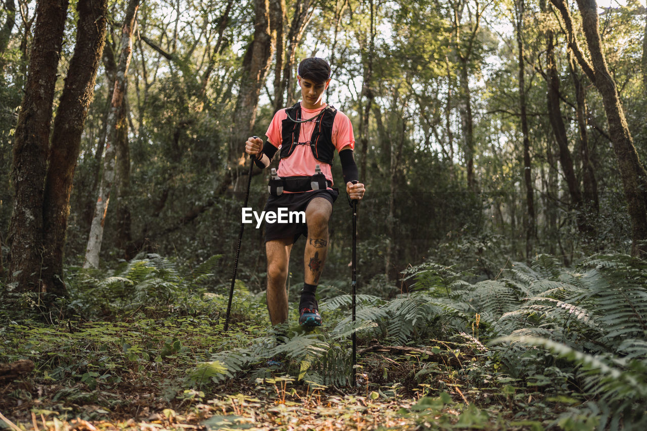 Man traveler with trekking poles walking up old stone stairs in jungles