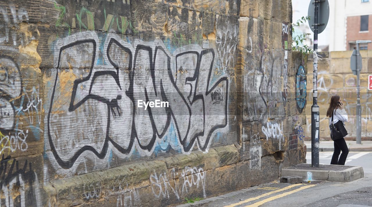 FULL LENGTH OF WOMAN WALKING IN GRAFFITI ON WALL