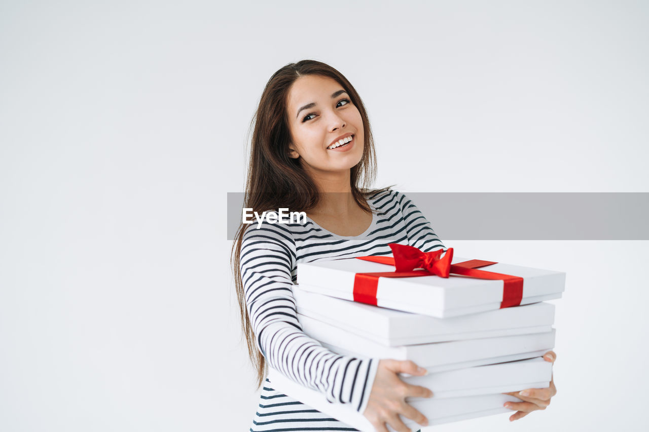 Portrait of young smiling asian woman with stack of gift boxes in hands on white background isolated