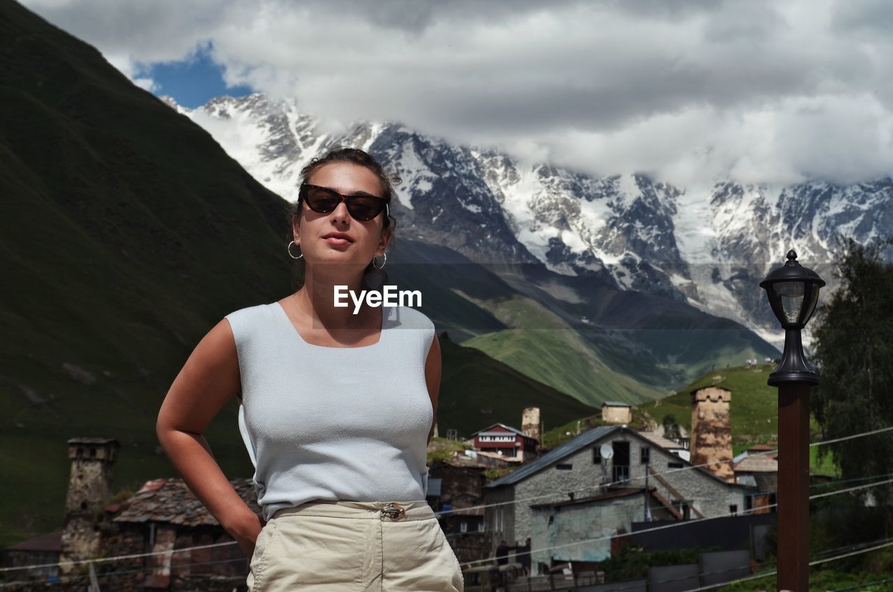 Young woman wearing sunglasses standing on mountain against sky
