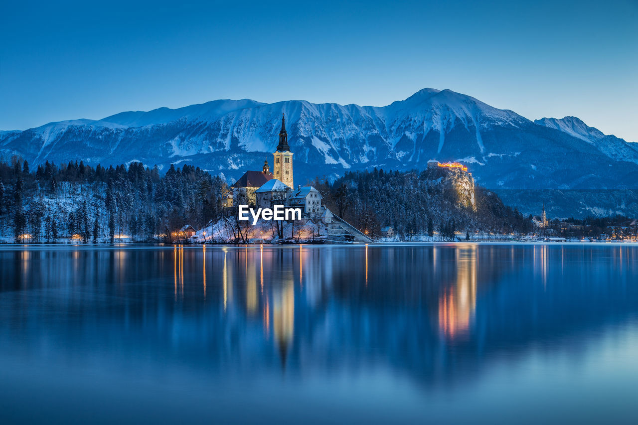 Bled castle in lake by mountains at dusk