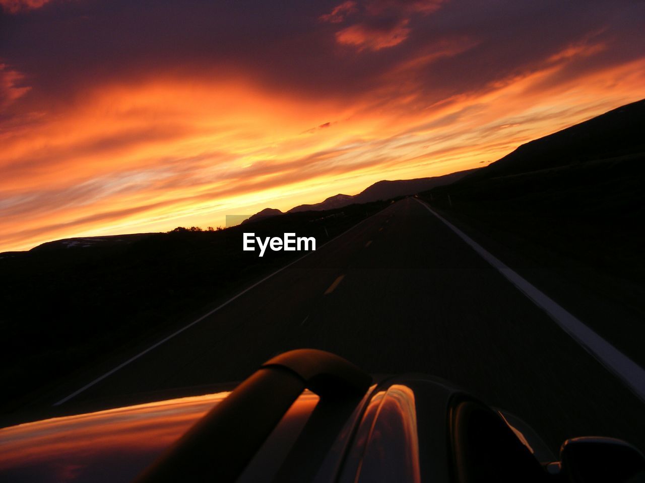 Cropped image of car on street against cloudy sky at sunset