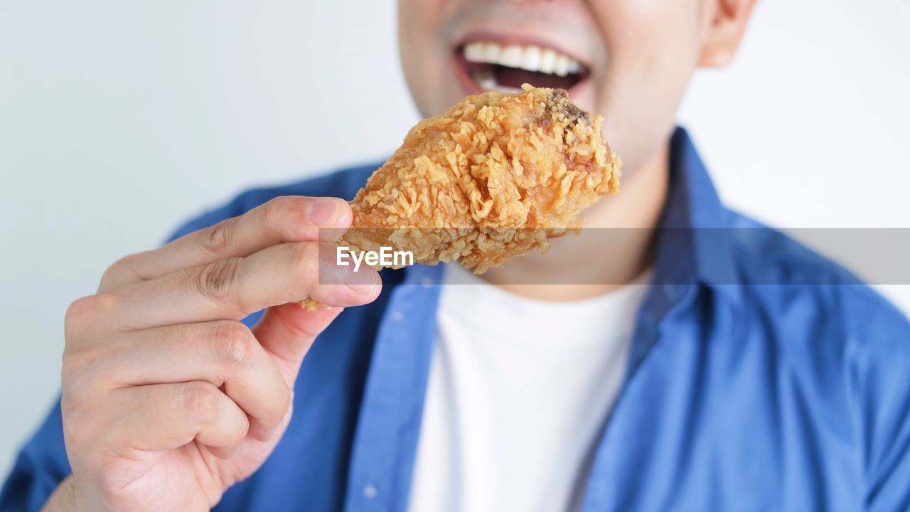 food, food and drink, eating, one person, unhealthy eating, men, holding, adult, fast food, indoors, meal, studio shot, close-up, biting, snack, bread, white background, human mouth, blue, sweet food, front view, portrait, hand, sandwich, hungry, person, enjoyment, emotion, headshot, baked, hamburger, happiness, young adult, sweet, lifestyles, freshness, casual clothing, take out food, smiling