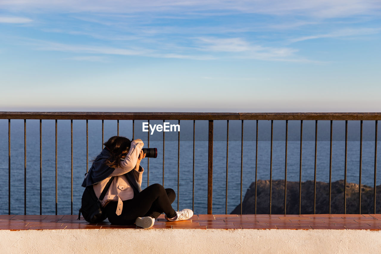 Beautiful women sitting and taking pictures on a cliff during sunset with copy space