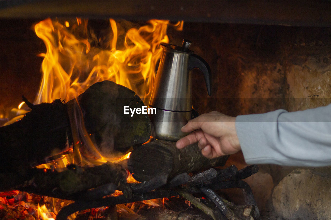 Close-up of hand holding kettle in fireplace