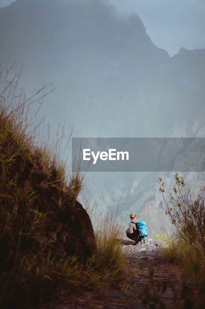 Rear view of woman crouching by cliff