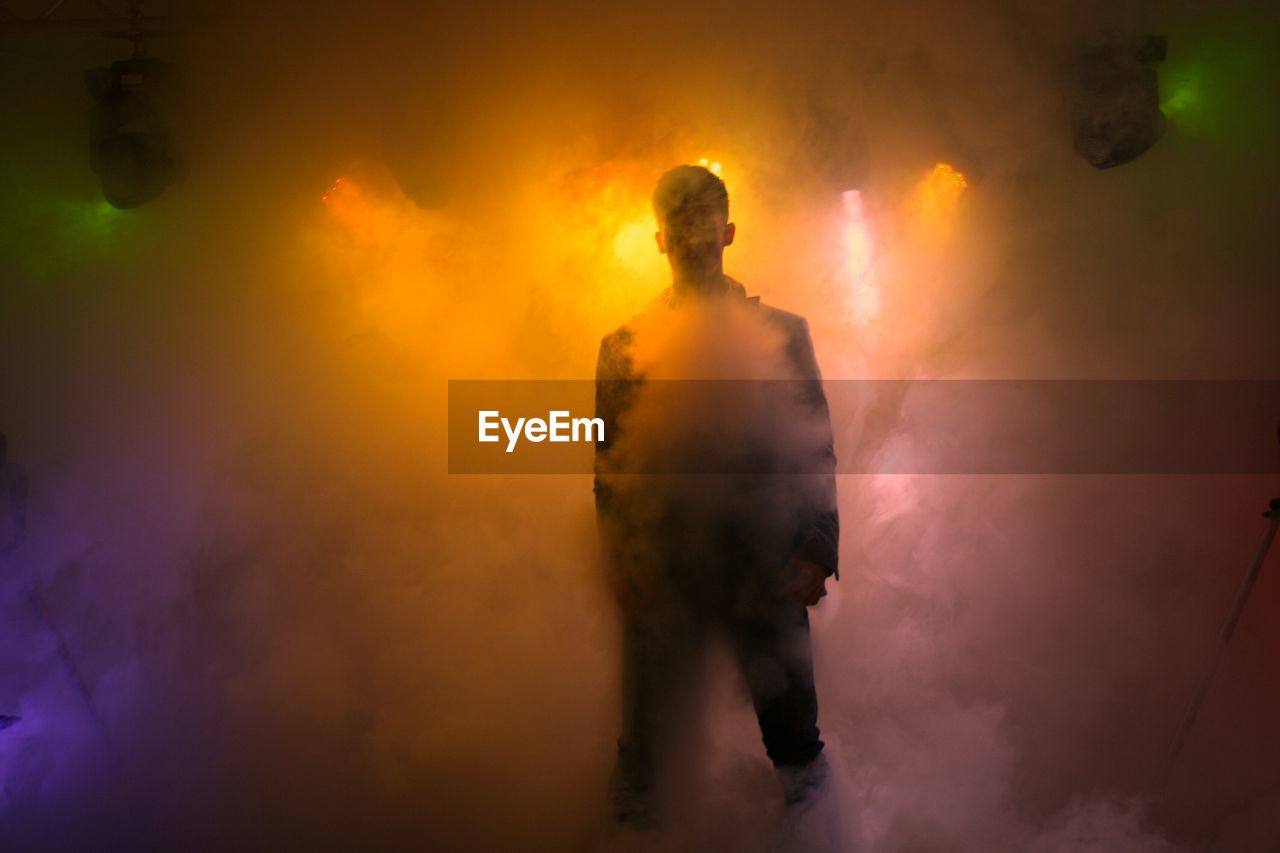 Man standing amidst illuminated smoke on stage