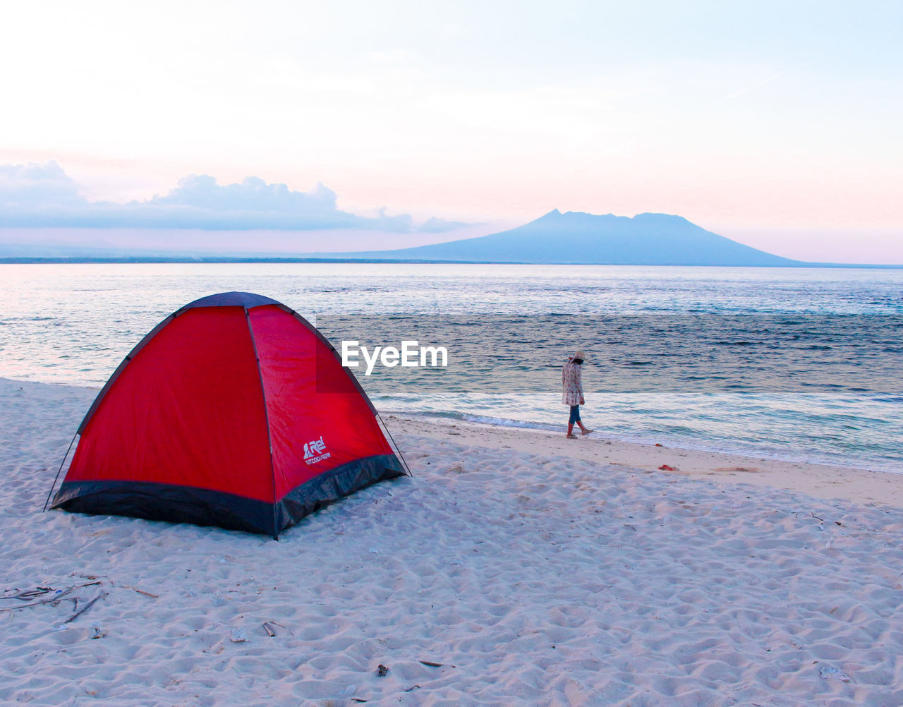 Rear view of young woman camping at beach against sky during sunset