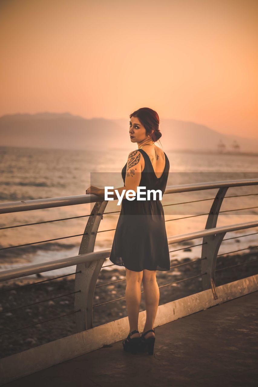 Portrait of woman standing at promenade against clear orange sky