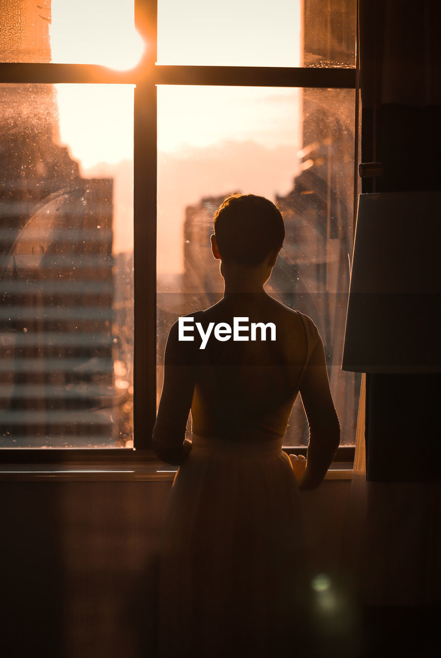 REAR VIEW OF SHIRTLESS MAN LOOKING THROUGH WINDOW AT GLASS