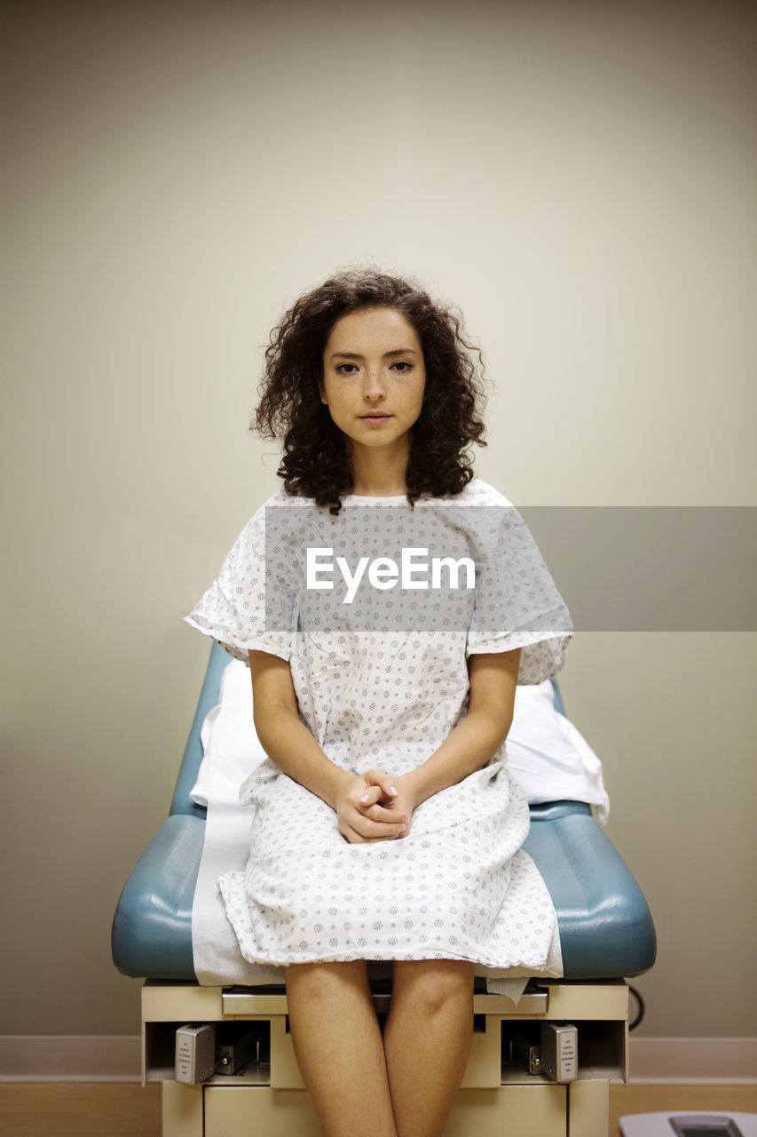 Portrait of woman with hands clasped sitting on bed in hospital