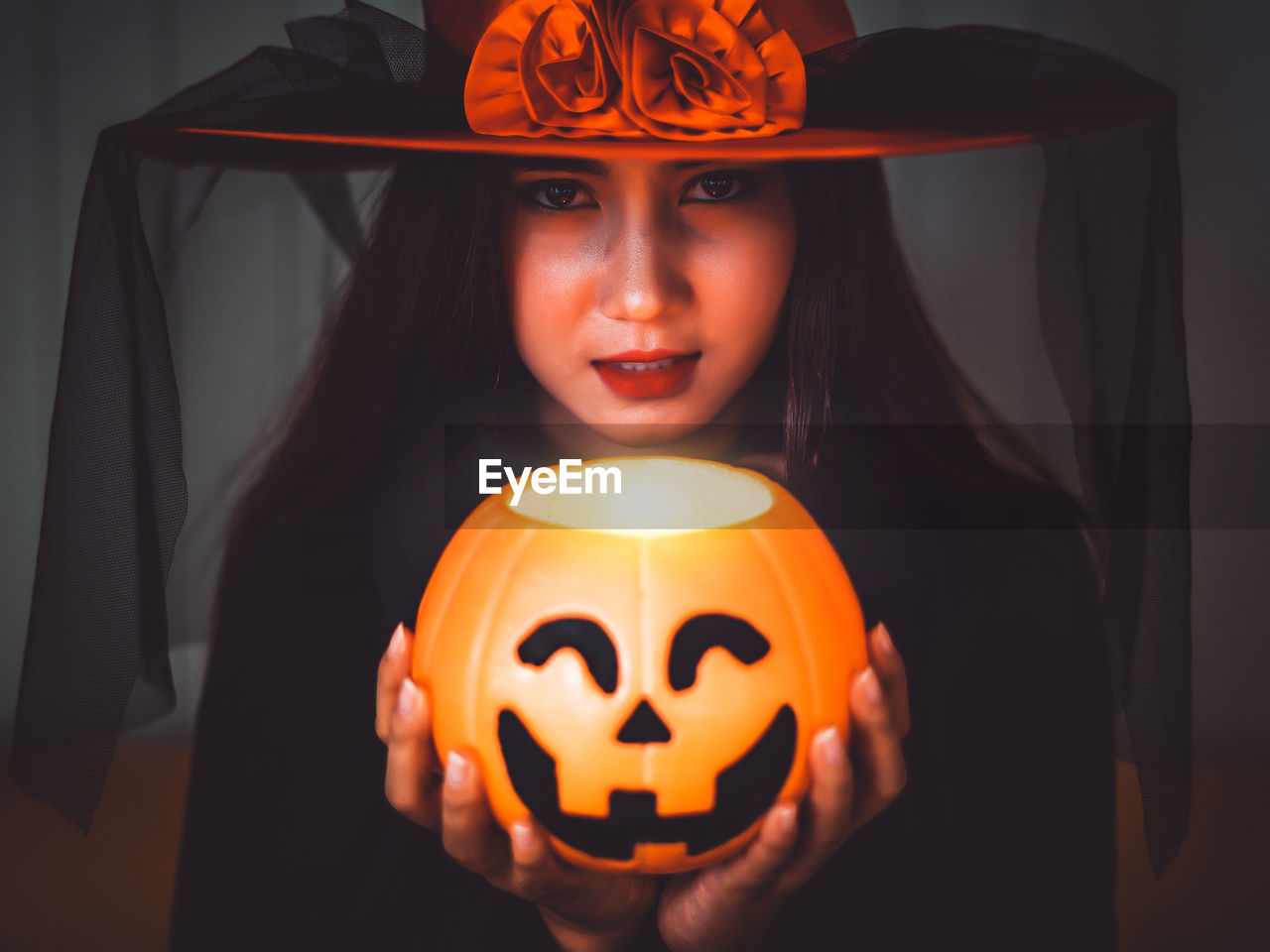 Portrait of young woman holding illuminated pumpkin against wall