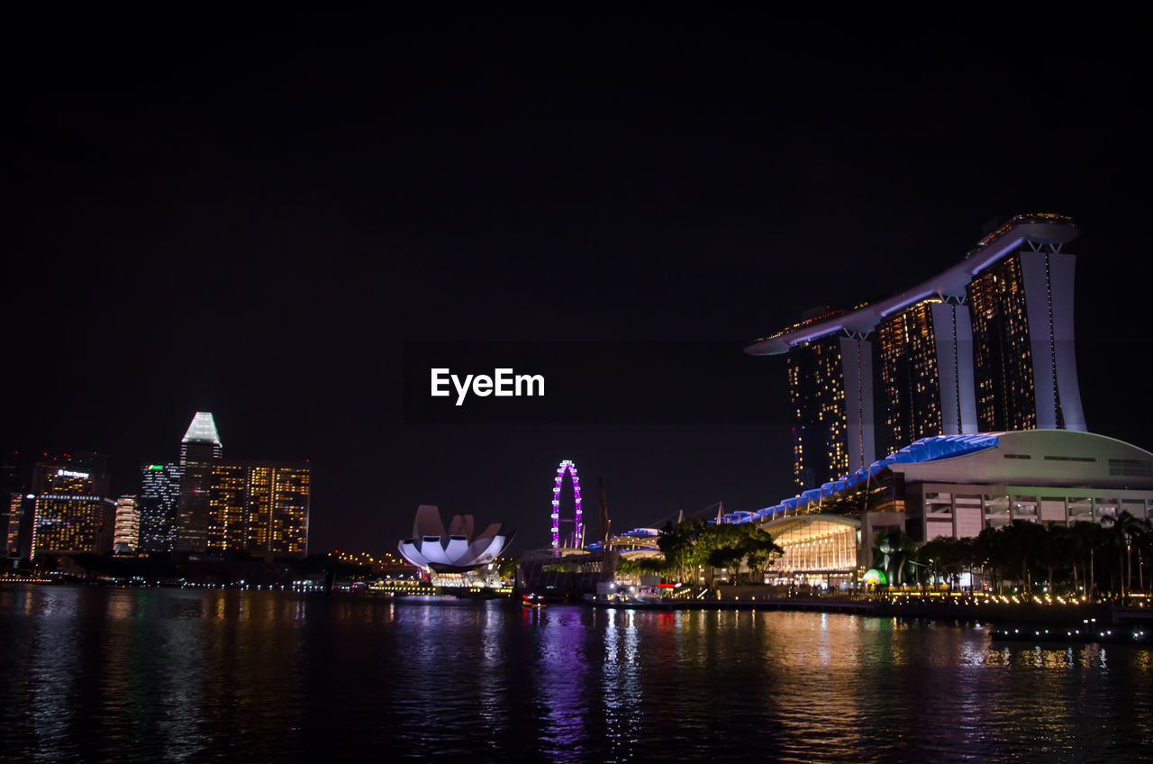 ILLUMINATED CITY BUILDINGS AT WATERFRONT