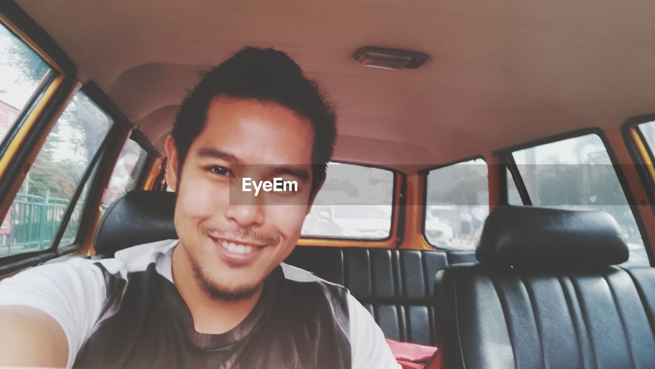 PORTRAIT OF SMILING YOUNG MAN IN CAR