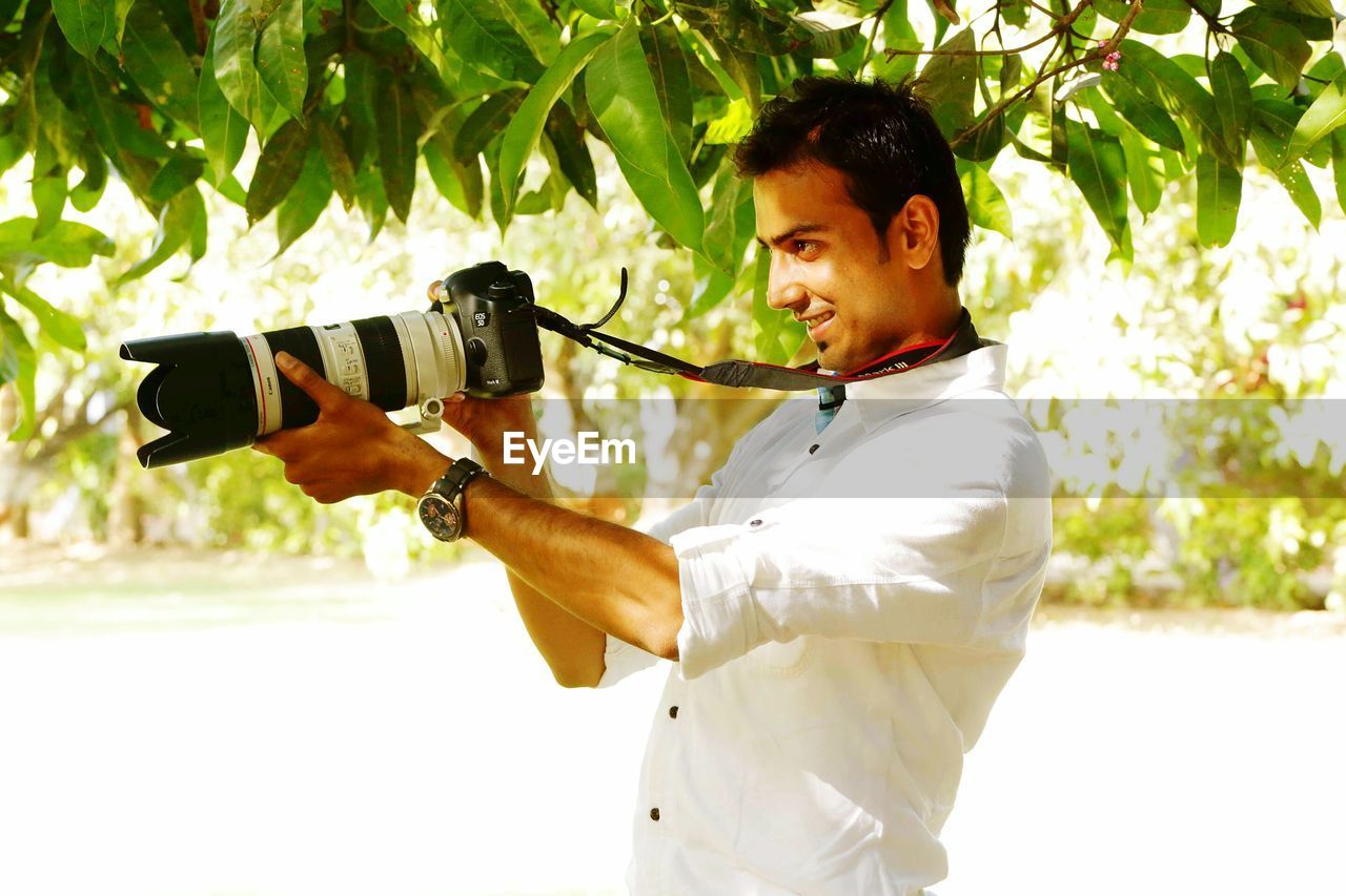 SIDE VIEW OF YOUNG MAN PHOTOGRAPHING WITH CAMERA