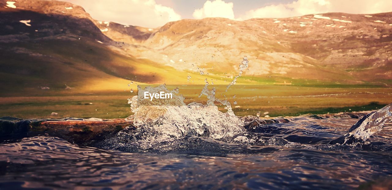 WATER SPLASHING ON ROCKS AGAINST SKY AT SUNSET