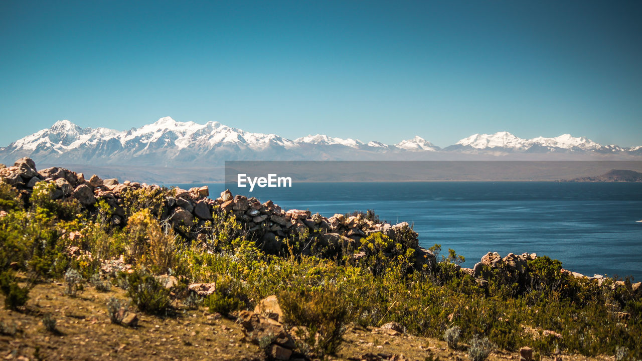 Scenic view of sea and mountains against clear blue sky