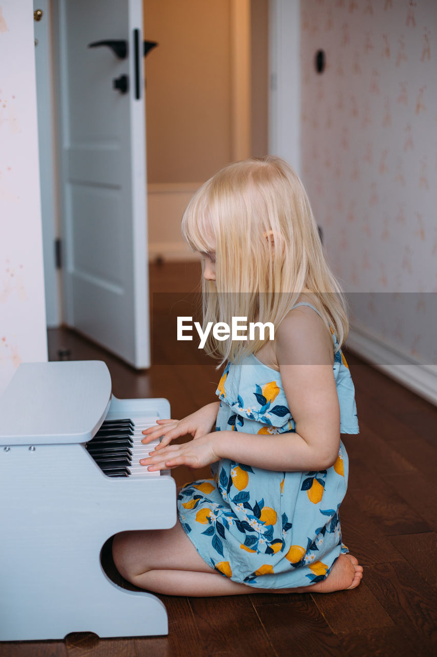 Little blonde girl plays a toy piano at home. musical development in childhood