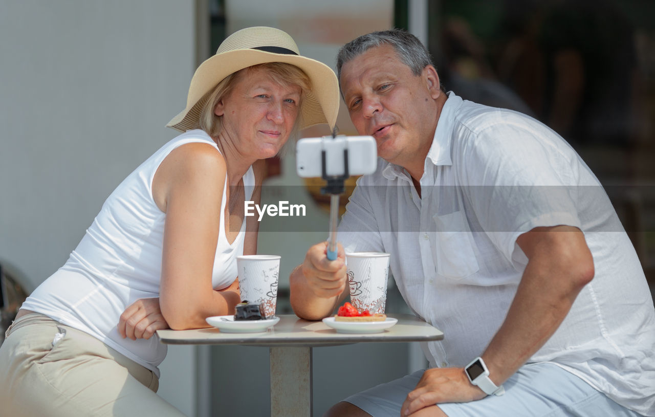Mature couple taking selfie while sitting at restaurant