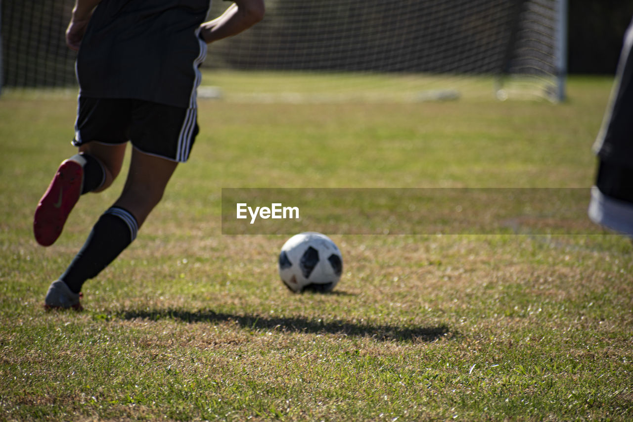 LOW SECTION OF WOMAN PLAYING SOCCER BALL ON FIELD