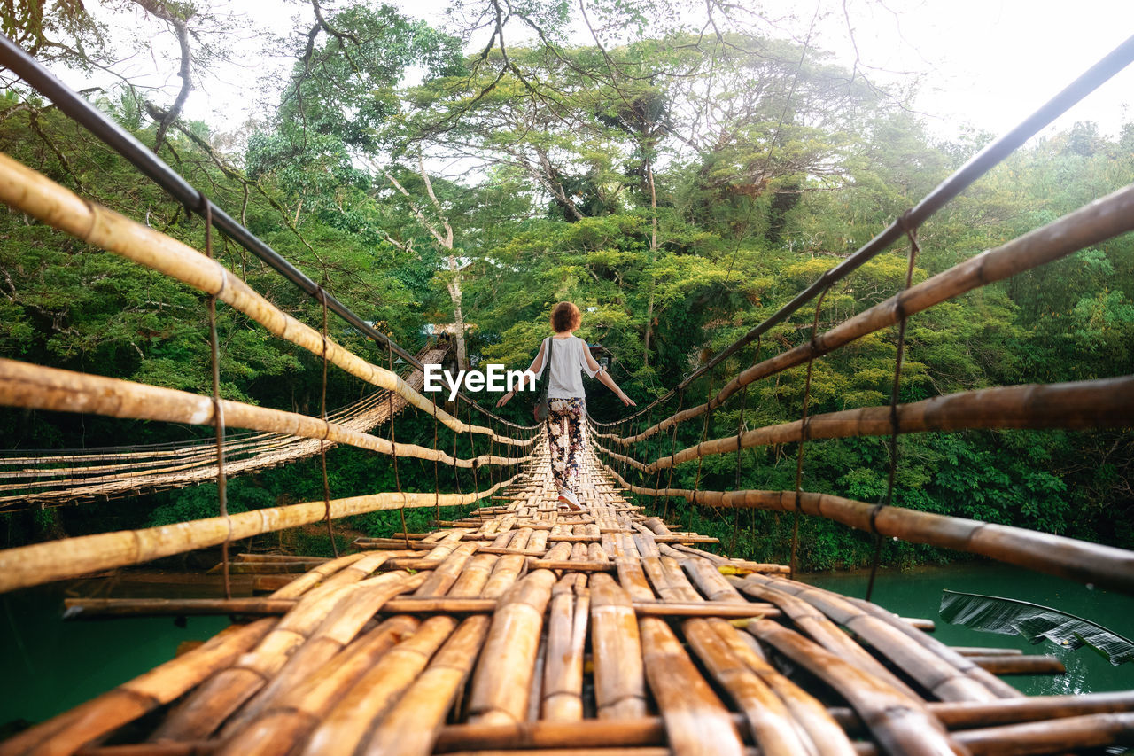 Rear view of woman walking on footbridge in forest