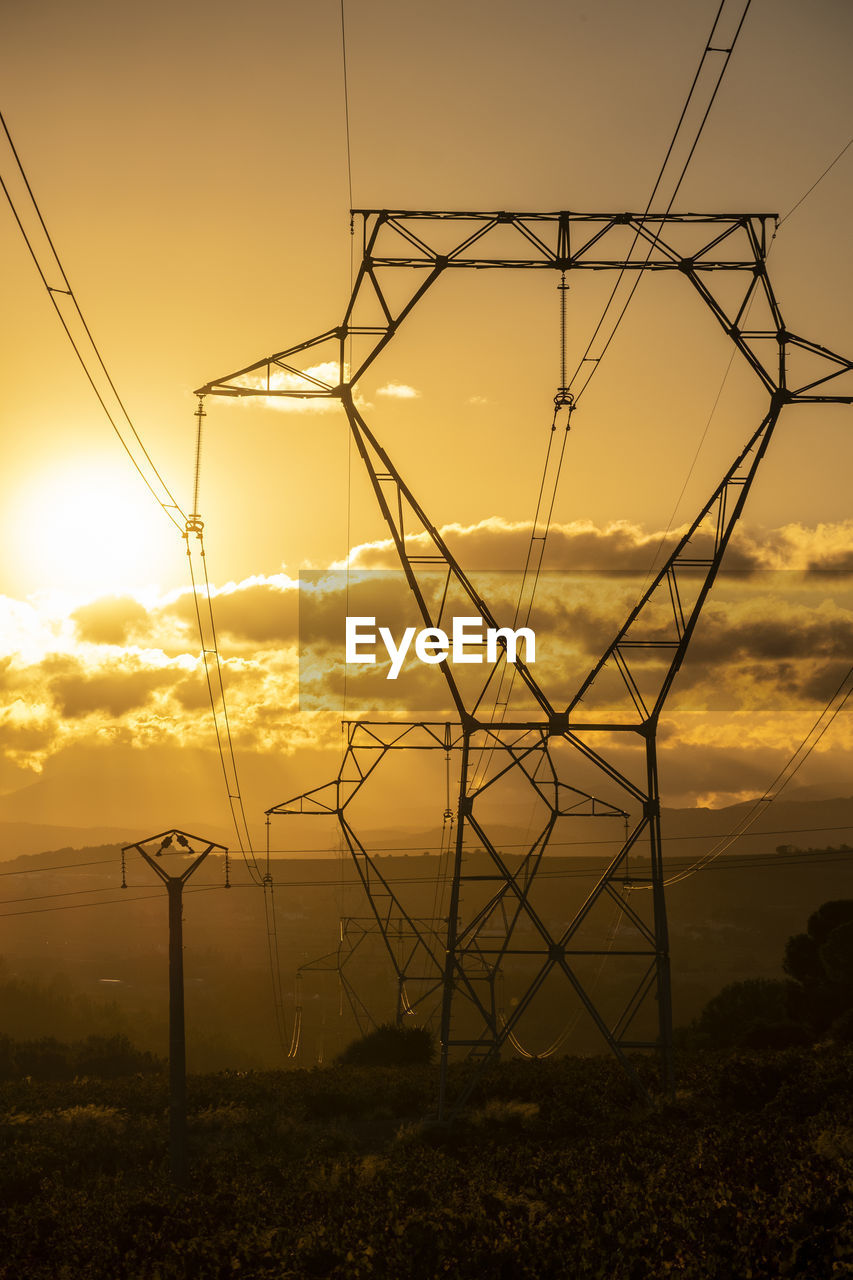 Low angle view of electricity pylon against sky during sunset