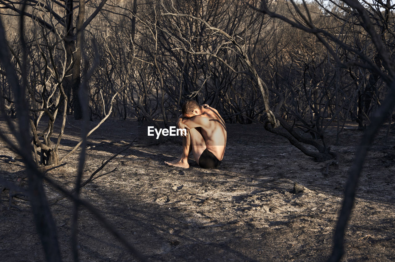 Man sitting in fetal position on burned forest floor